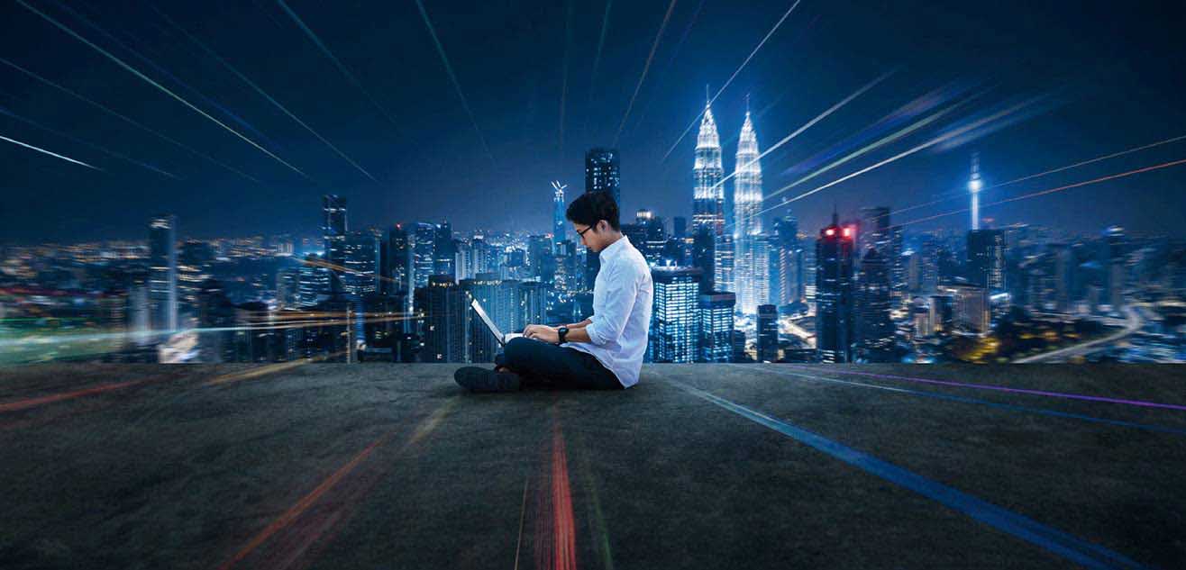 A man sitting on the floor using laptop with night view A man sitting on the floor using laptop with night view